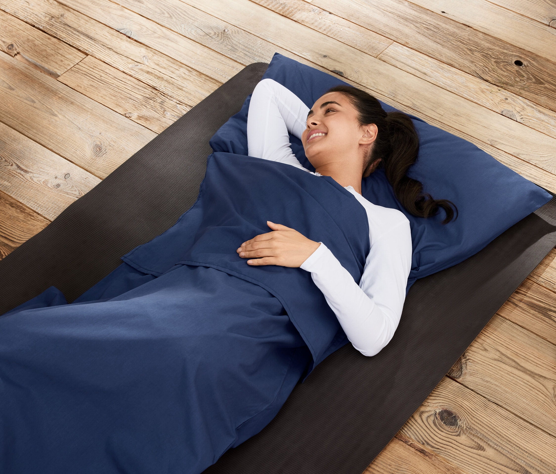 Kobieta leży we wkładzie do śpiwora na macie na drewnianej podłodze.