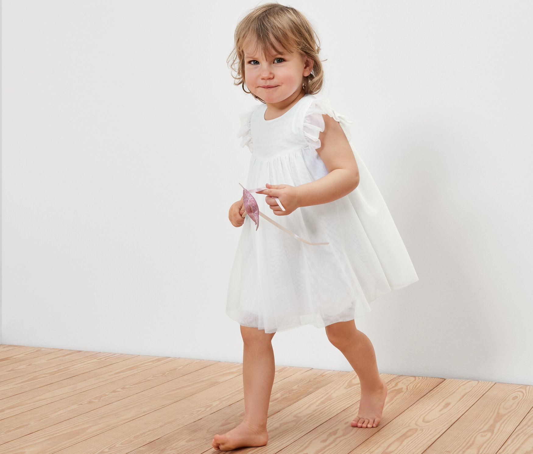 Dziewczynka w tiulowej sukience idzie po drewnianej podłodze.