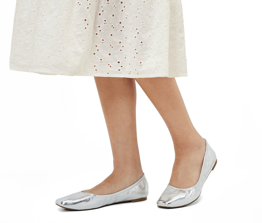 Nogi kobiety w białej sukience i balerinach skórzanych.