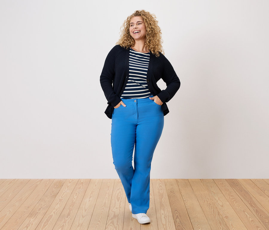 Kobieta z kręconymi włosami w granatowym kardiganie, w paski i niebieskich spodniach.