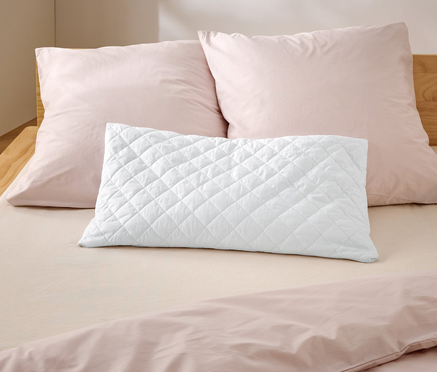 Na łóżku leżą dwie różowe poduszki i jedna biała, pikowana.