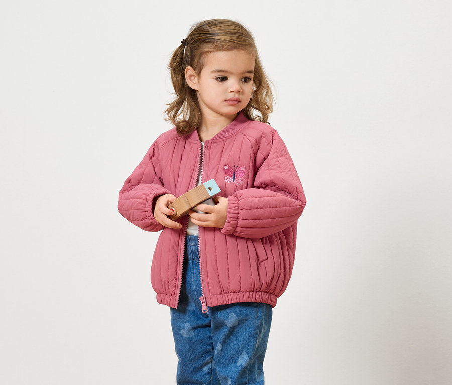 Dziewczynka w różowej kurtce trzyma drewnianą zabawkę.