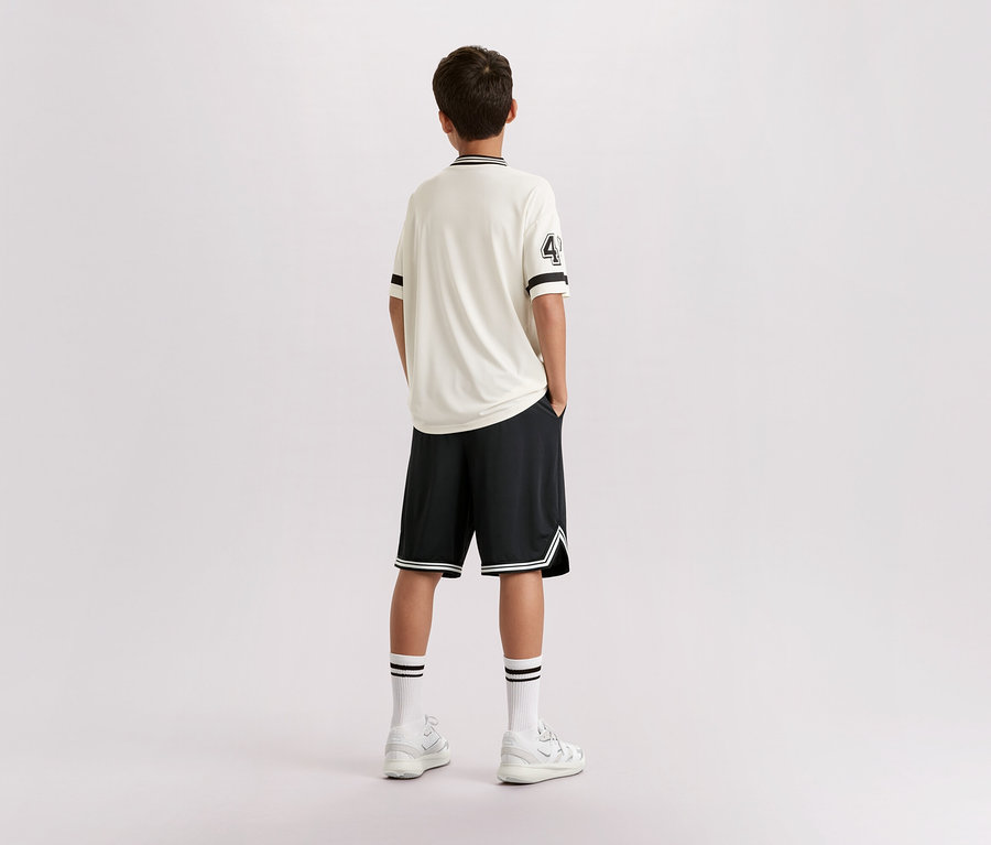 Chłopak stoi tyłem do kamery, ma na sobie jasną koszulkę z numerem 4, czarne szorty, białe skarpetki i tenisówki.