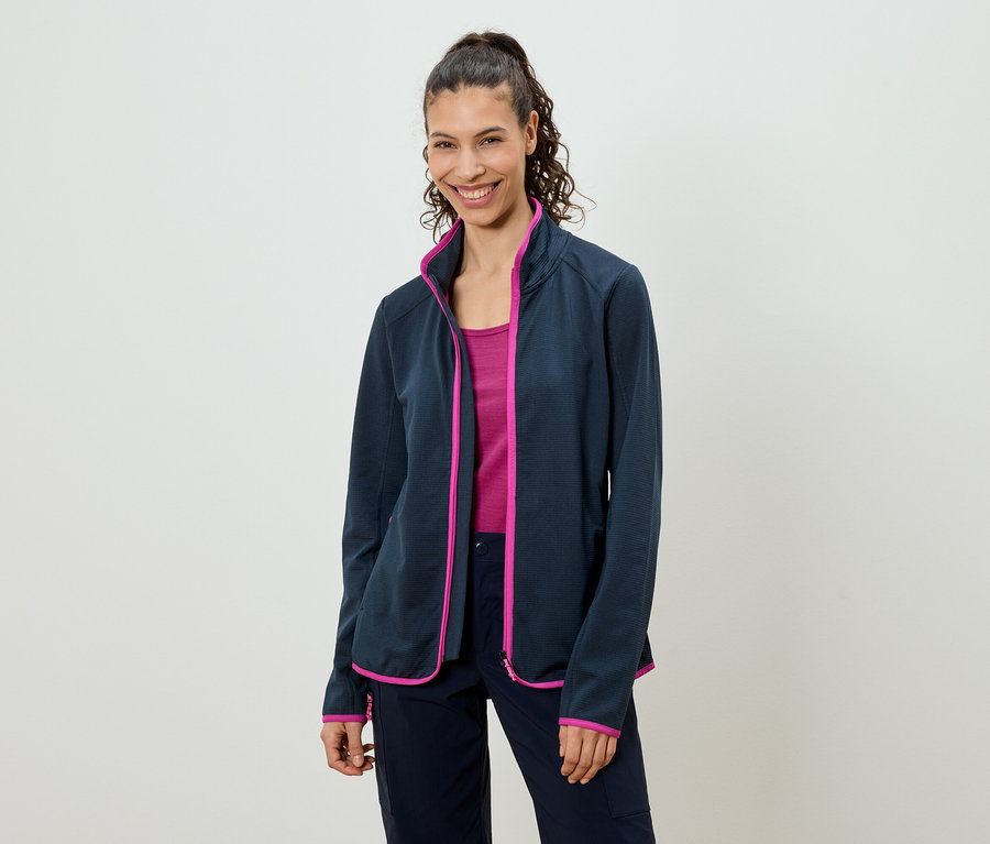 Kobieta z końskim ogonem ma na sobie granatową kurtkę polarową z różowymi akcentami, różowy top i granatowe spodnie.