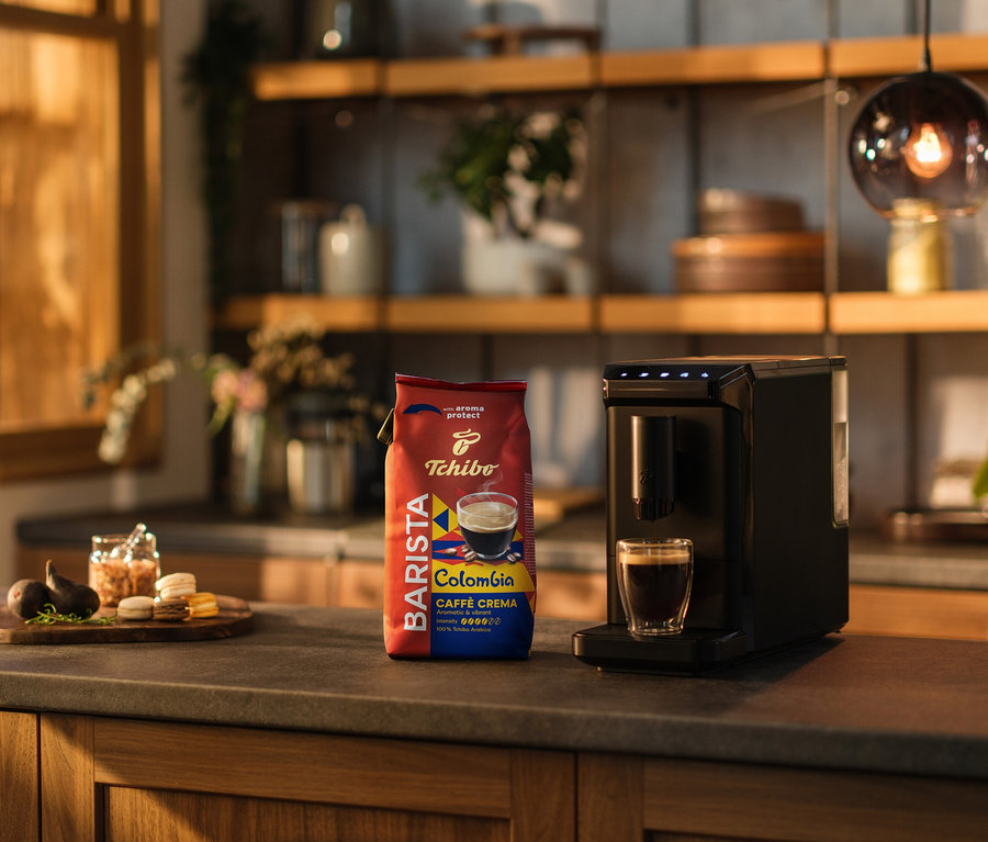 Na blacie kuchennym stoi ekspres do kawy, filiżanka kawy i opakowanie kawy ziarnistej BARISTA Origins Colombia – 1 kg.