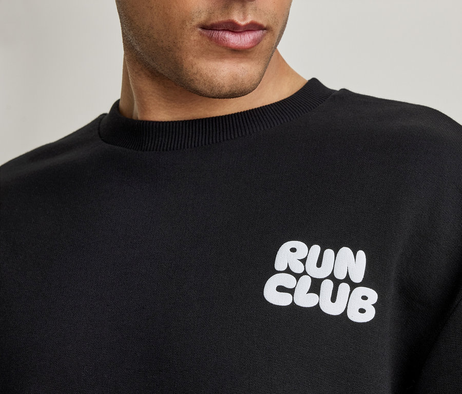 Zbliżenie na mężczyznę w czarnej bluzie z białym napisem 'RUN CLUB'.