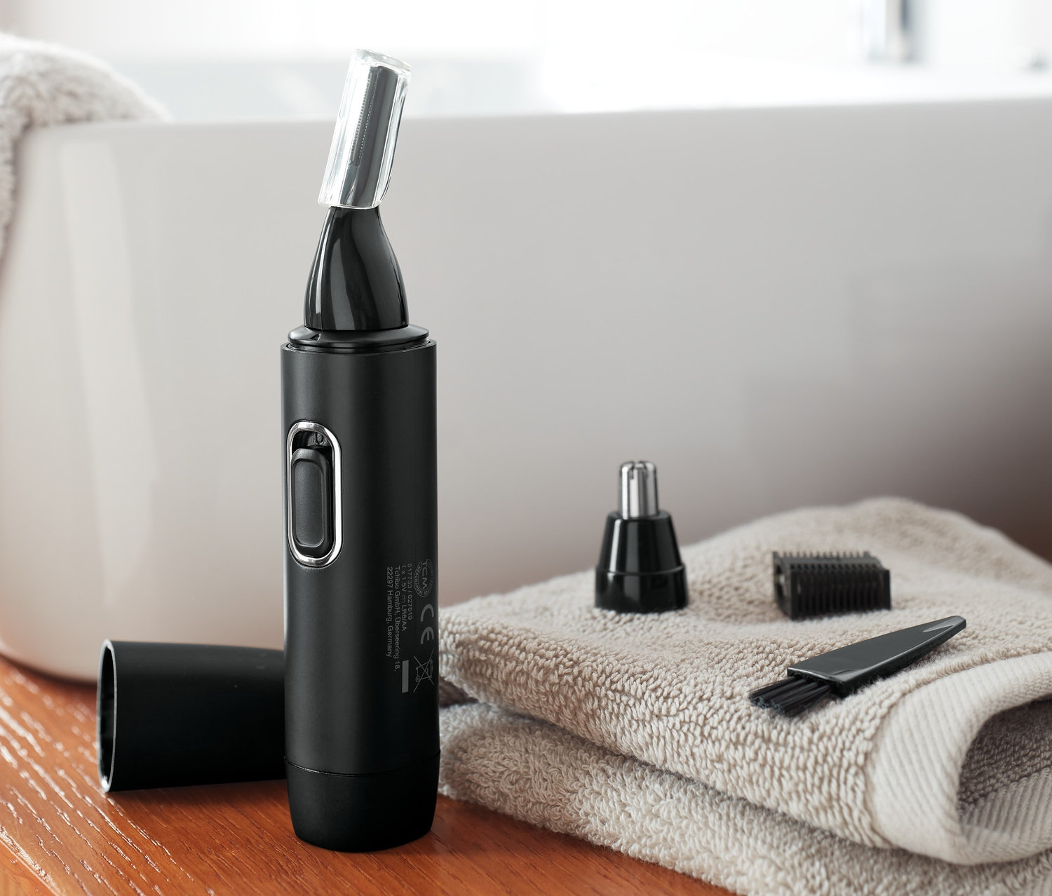 Czarny trymer do nosa i uszu z nasadkami leży na ręczniku w łazience.