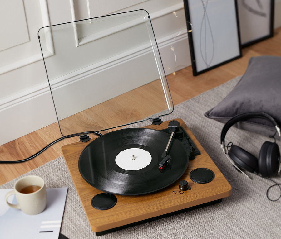 Gramofon »Dual DTR 61« z wbudowanymi głośnikami odtwarza płytę. Obok stoi kubek i słuchawki.