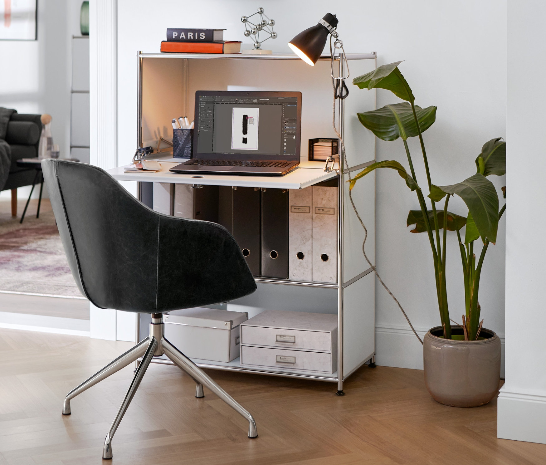 Obrotowy fotel ze sztucznej skóry z wyściełanym siedziskiem stoi przy białym metalowym sekretarzyku »CN3« z lampą na zacisk.