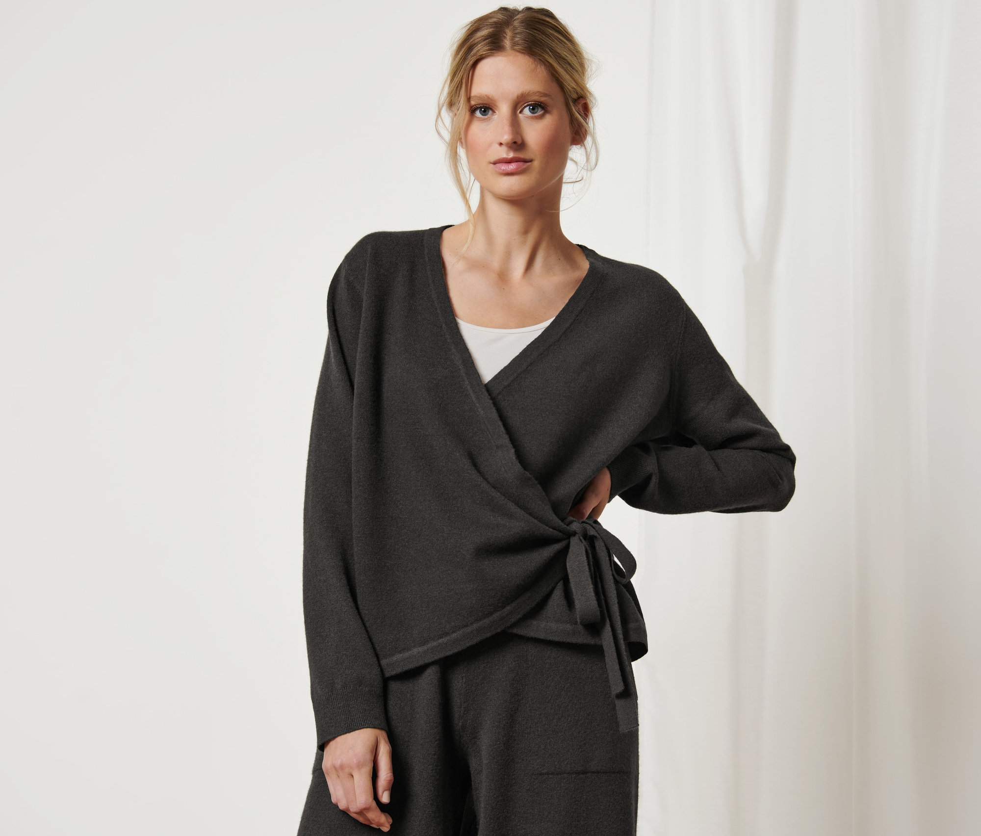 Kobieta pozuje w swetrze kopertowym.