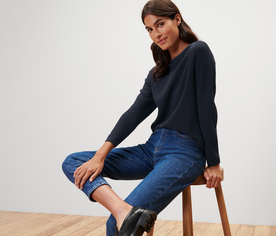 Kobieta siedzi na stołku i ma na sobie granatowy sweter z dzianiny.