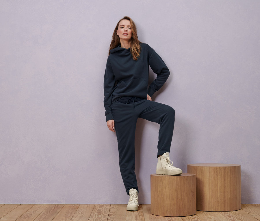 Kobieta pozuje w granatowej bluzie z kapturem, spodniach dresowych i ocieplanych butach typu sneakers ze skóry.