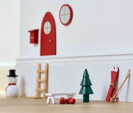 Miniaturowa dekoracja świąteczna: czerwone drzwi, okno, choinka, narty i bałwan.