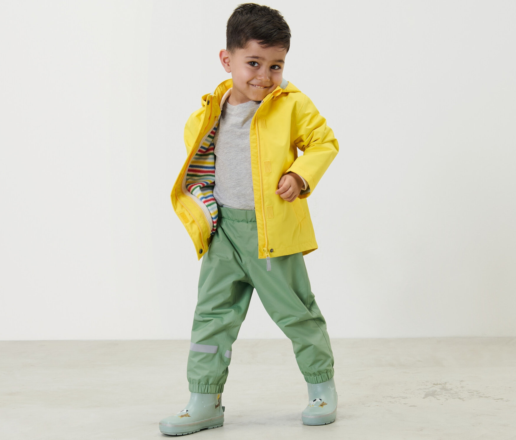 Chłopiec pozuje w trawiastozielonych spodniach przeciwdeszczowych i żółtej kurtce przeciwdeszczowej.