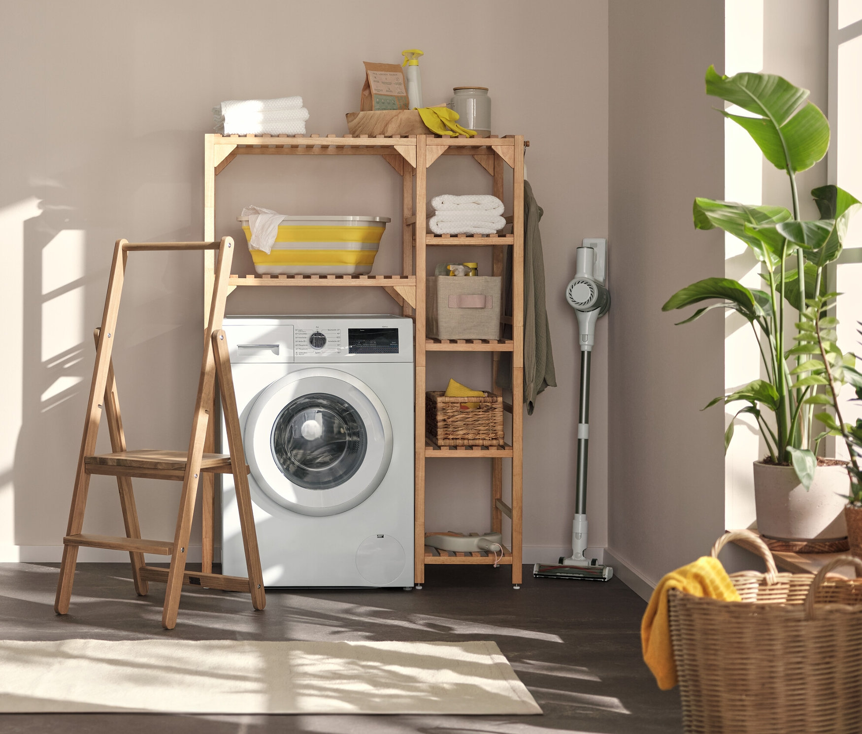 W pralni stoi pralka, nad nią szafka na pralkę z elementem bocznym, a po lewej stronie półka z ruchomymi haczykami i podstawą oraz drabina schodkowa z litego drewna.
