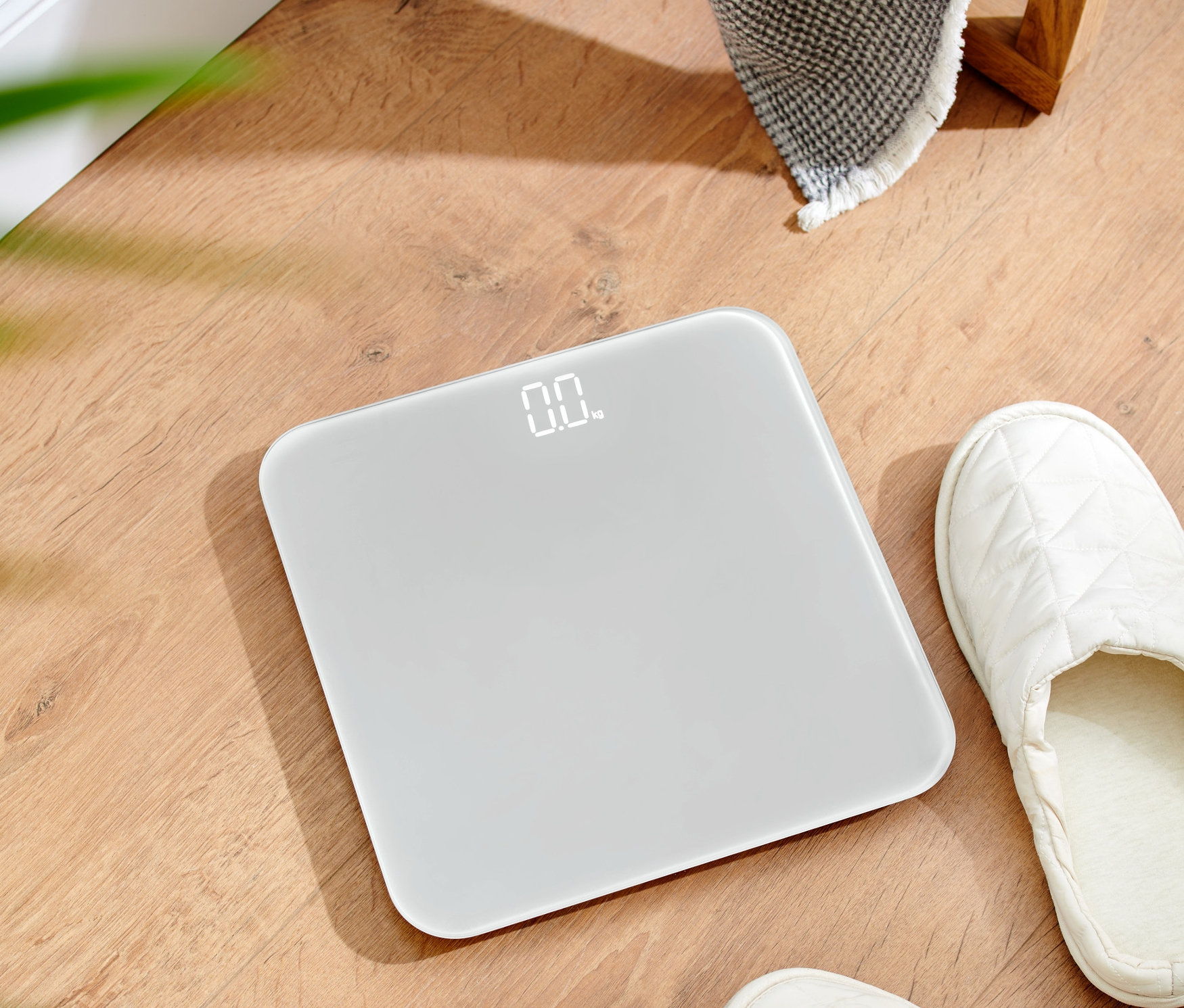 Kompaktowa waga łazienkowa leży na drewnianej podłodze.
