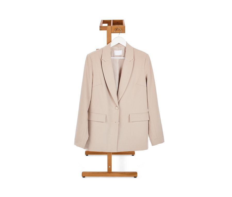 Beżowy blezer wisi na wieszaku stojącym na ubrania.