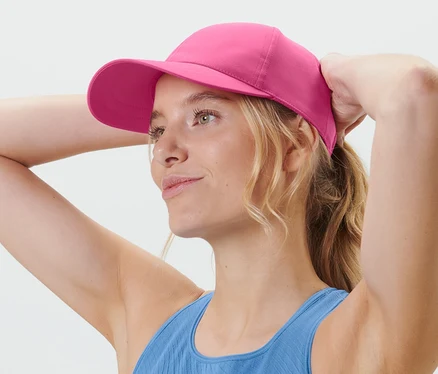 Blondynka poprawia różową sportową czapkę z daszkiem.