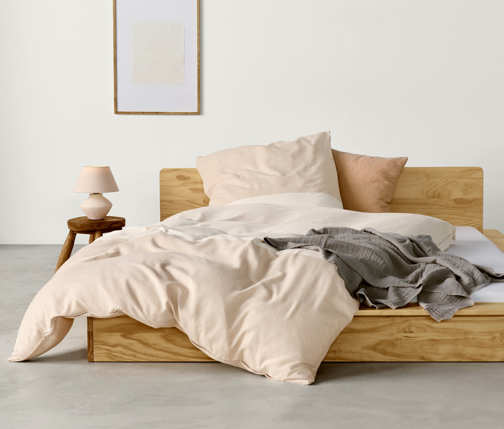 Sypialnia z drewnianym łóżkiem, beżową pościelą flanelową w rozmiarze standardowym i niestandardowym oraz szarym kocem.