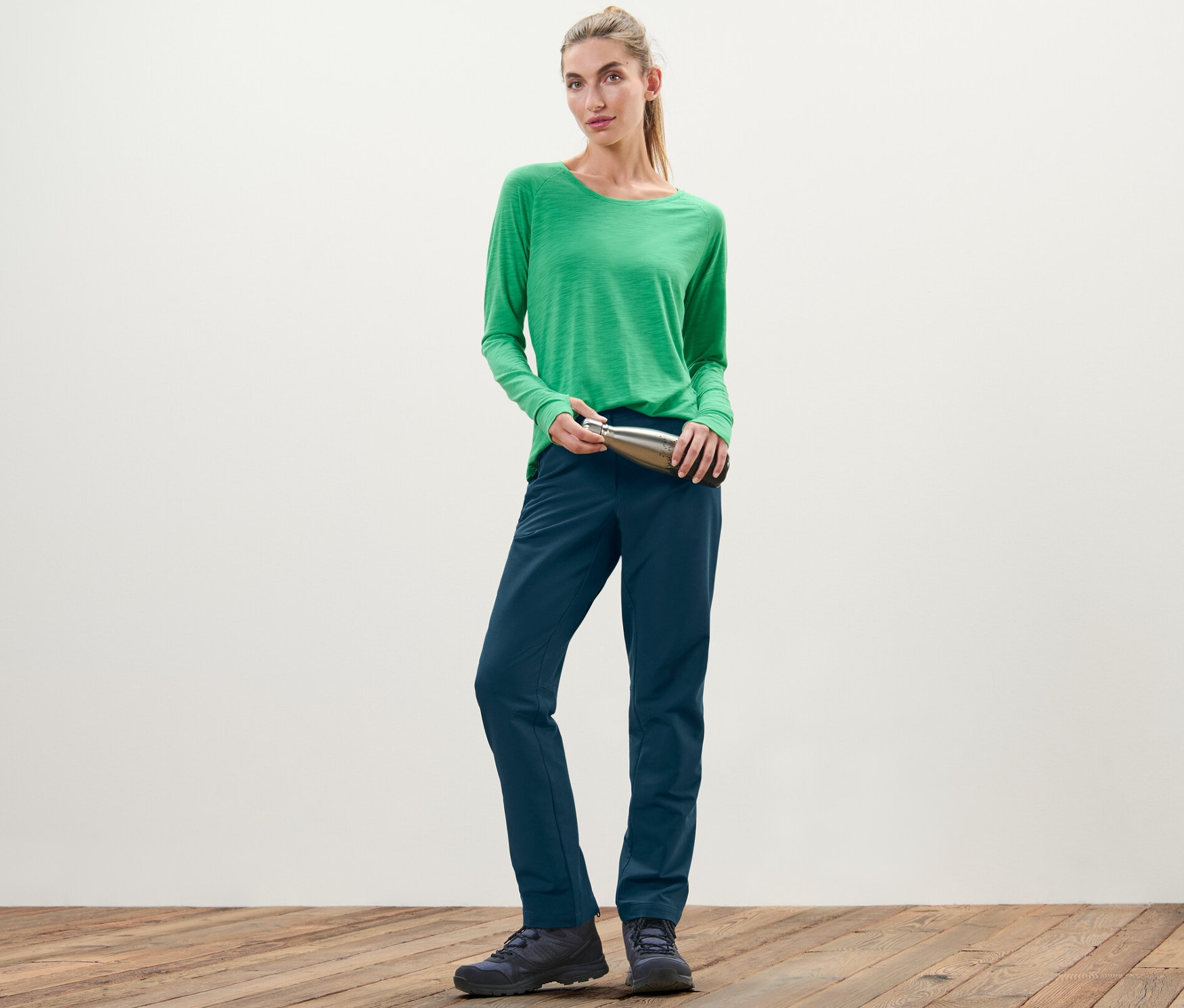 Kobieta w zielonej koszulce trzyma srebrną butelkę i ma na sobie spodnie z softshellu.
