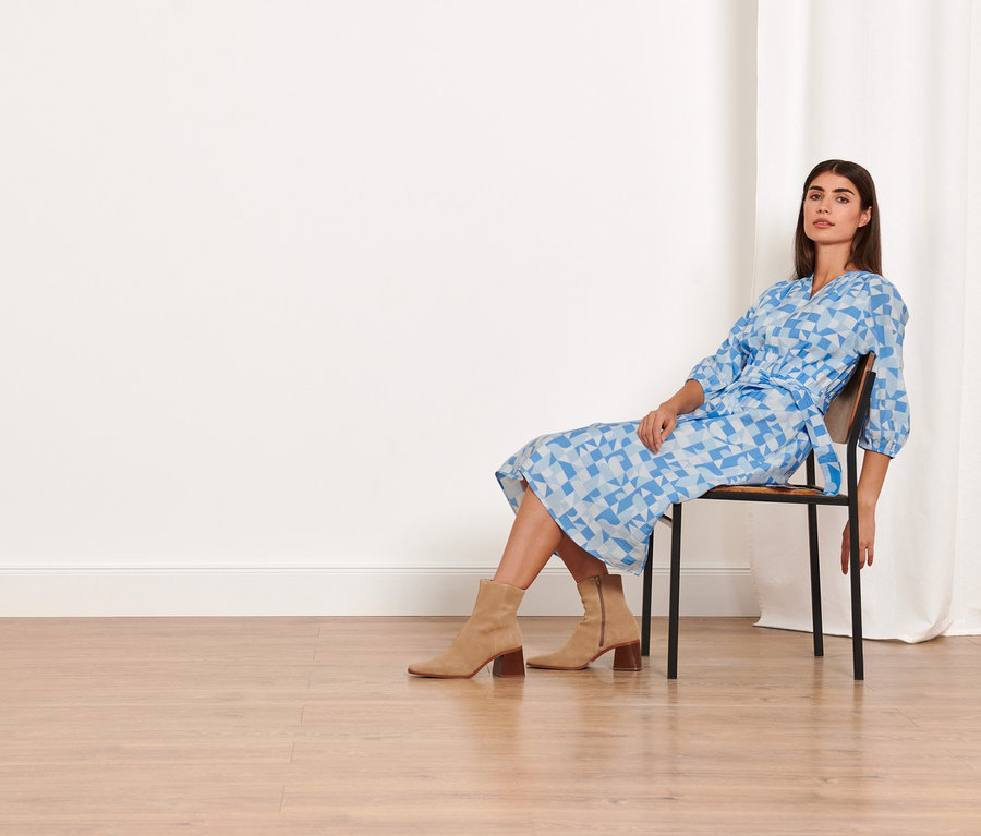 Kobieta siedzi na krześle i ma na sobie sukienkę z tkaniny z nadrukiem.