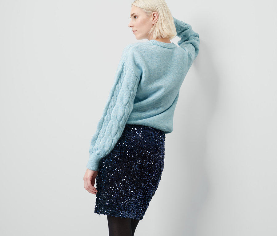 Kobieta pozuje w swetrze i spódnicy z cekinami.