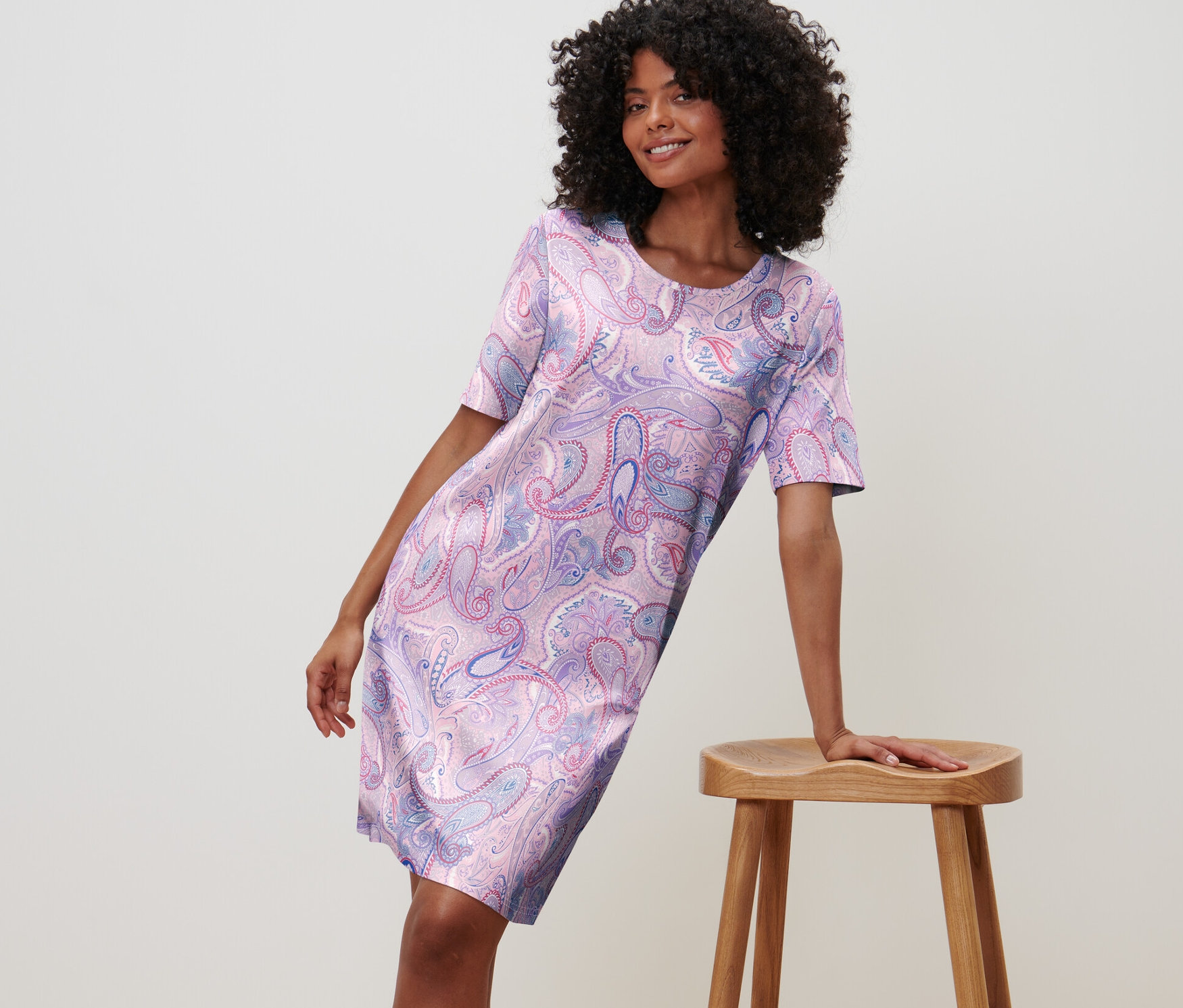 Kobieta opiera się o stołek w koszuli nocnej w kwiatowy wzór.