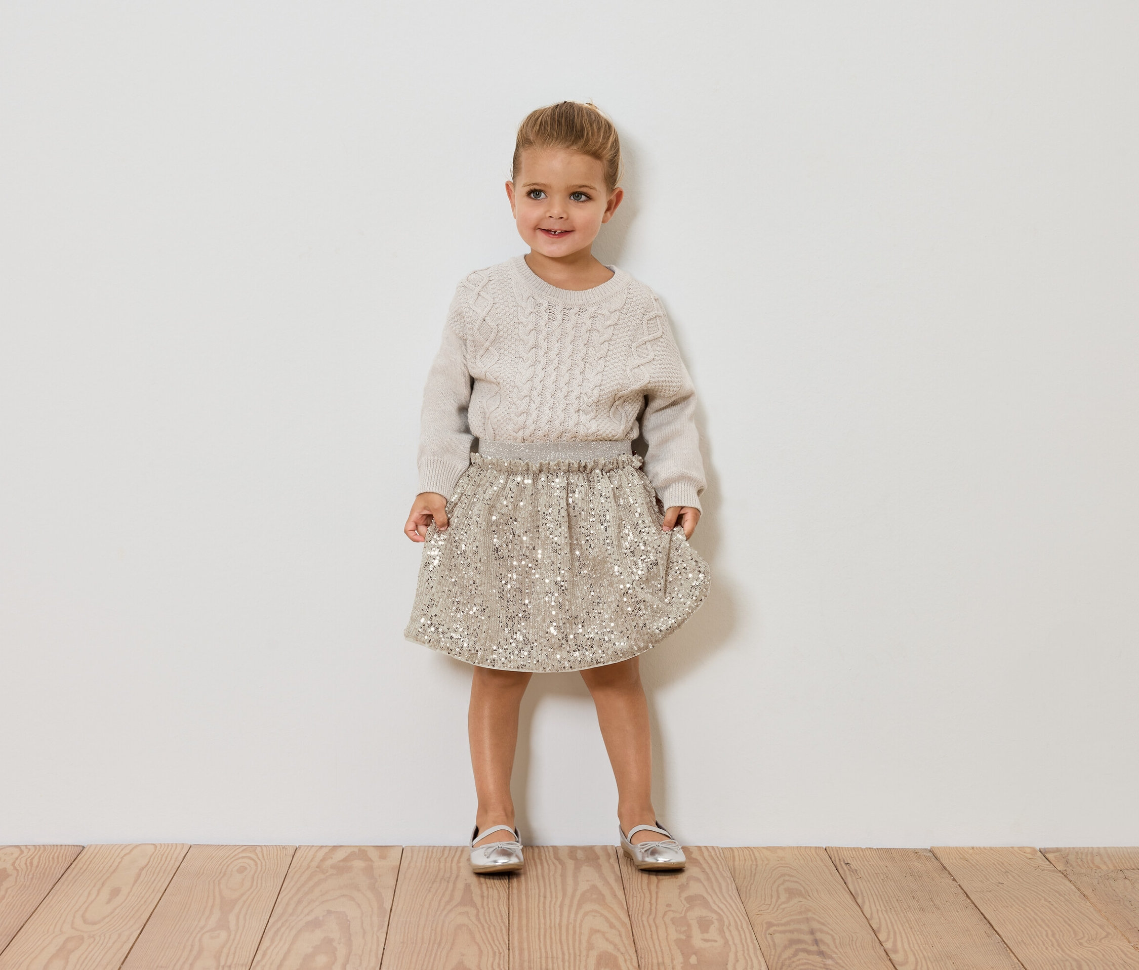 Dziewczynka stoi i ma na sobie sweter i spódnicę.