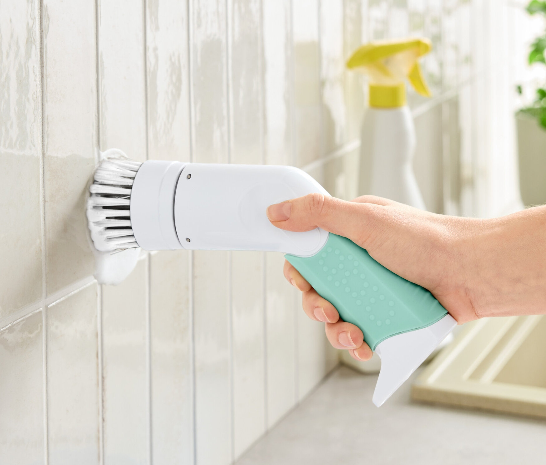 Ręka trzyma elektryczną szczotkę czyszczącą i czyści nią białe kafelki.