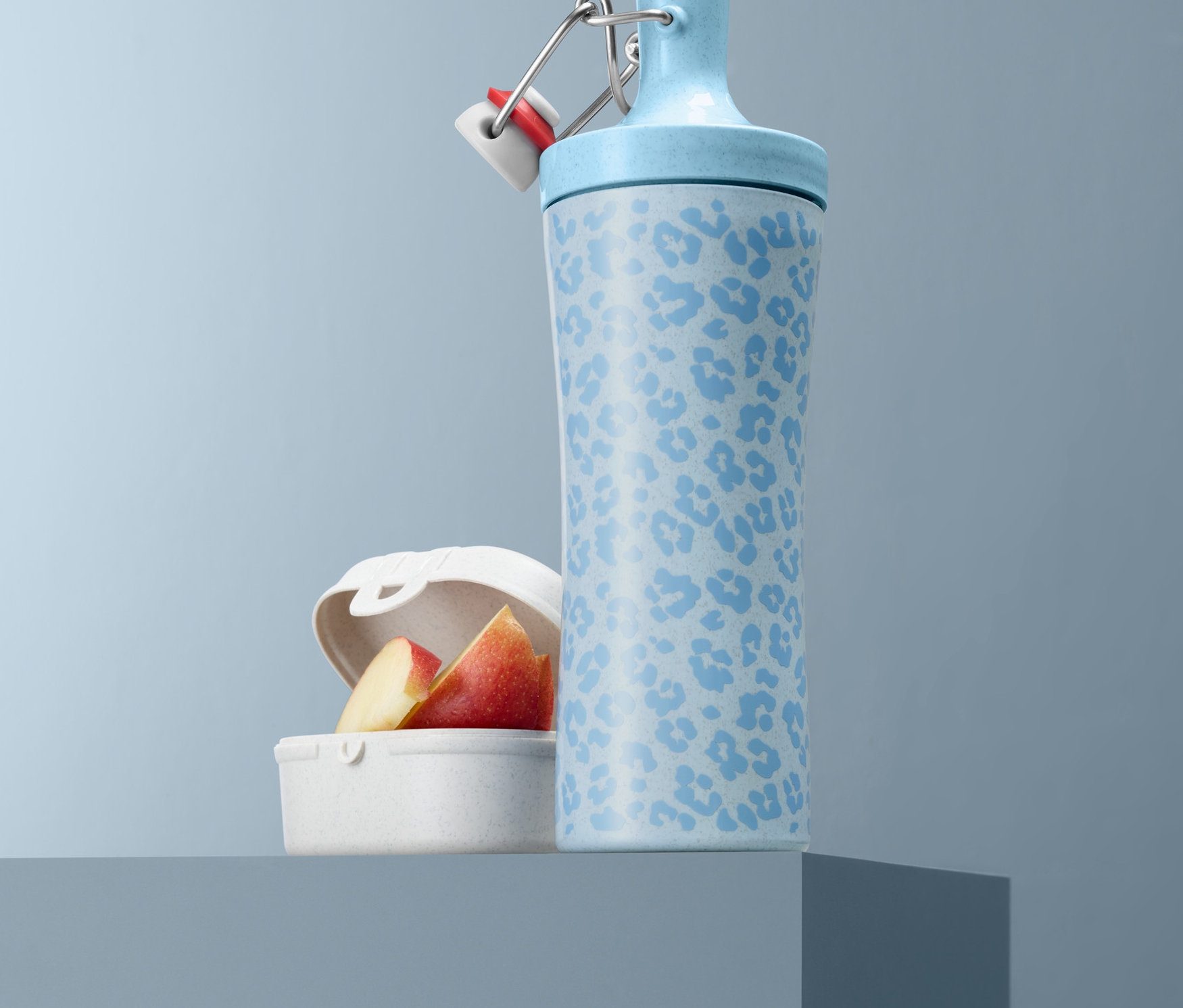 Jasnoniebieski bidon KOZIOL we wzory i jabłka w białym pudełku na lunch.