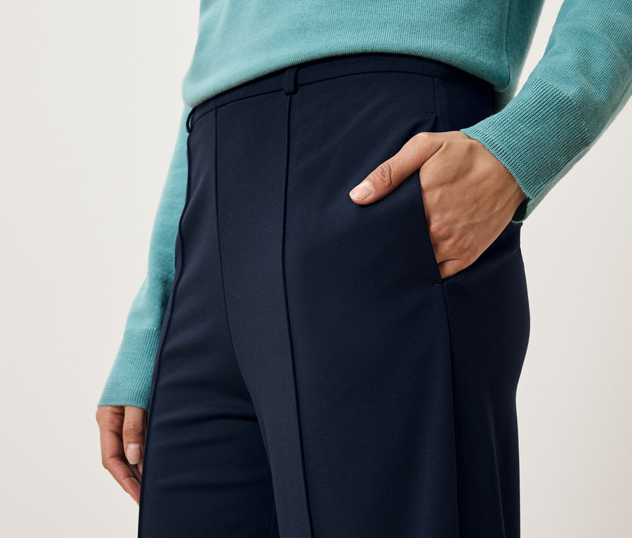 Zbliżenie na kobietę w niebieskich spodniach i swetrze z ręką w kieszeni.