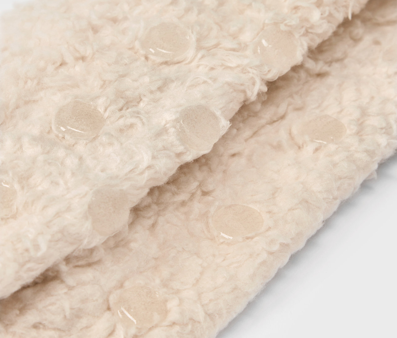 Szczegół beżowej, puszystej tkaniny z elementami antypoślizgowymi.