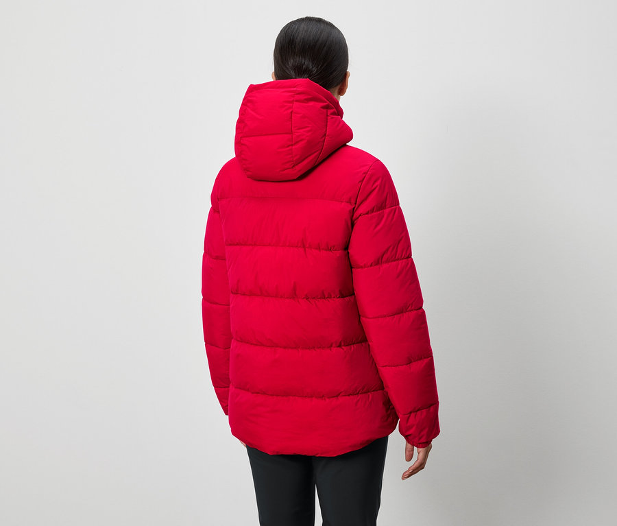 Osoba tyłem do kamery ma na sobie czerwoną puchową kurtkę z kapturem i czarne spodnie.
