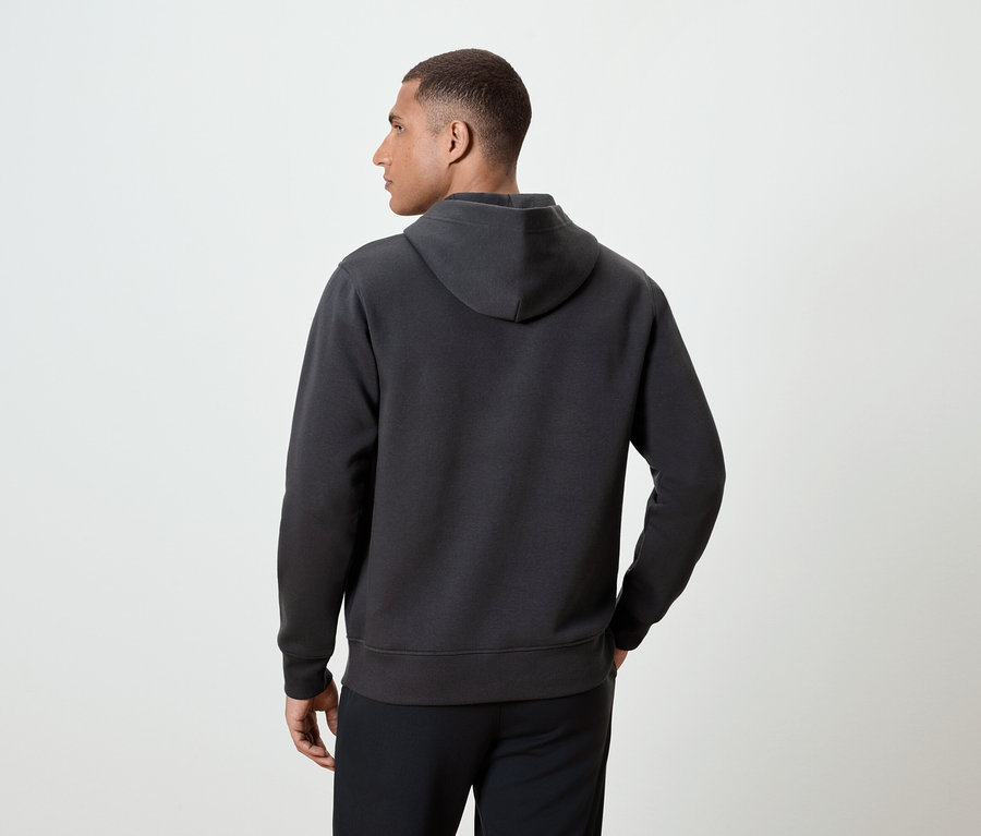 Mężczyzna tyłem do kamery ma na sobie ciemnoszarą bluzę z kapturem.