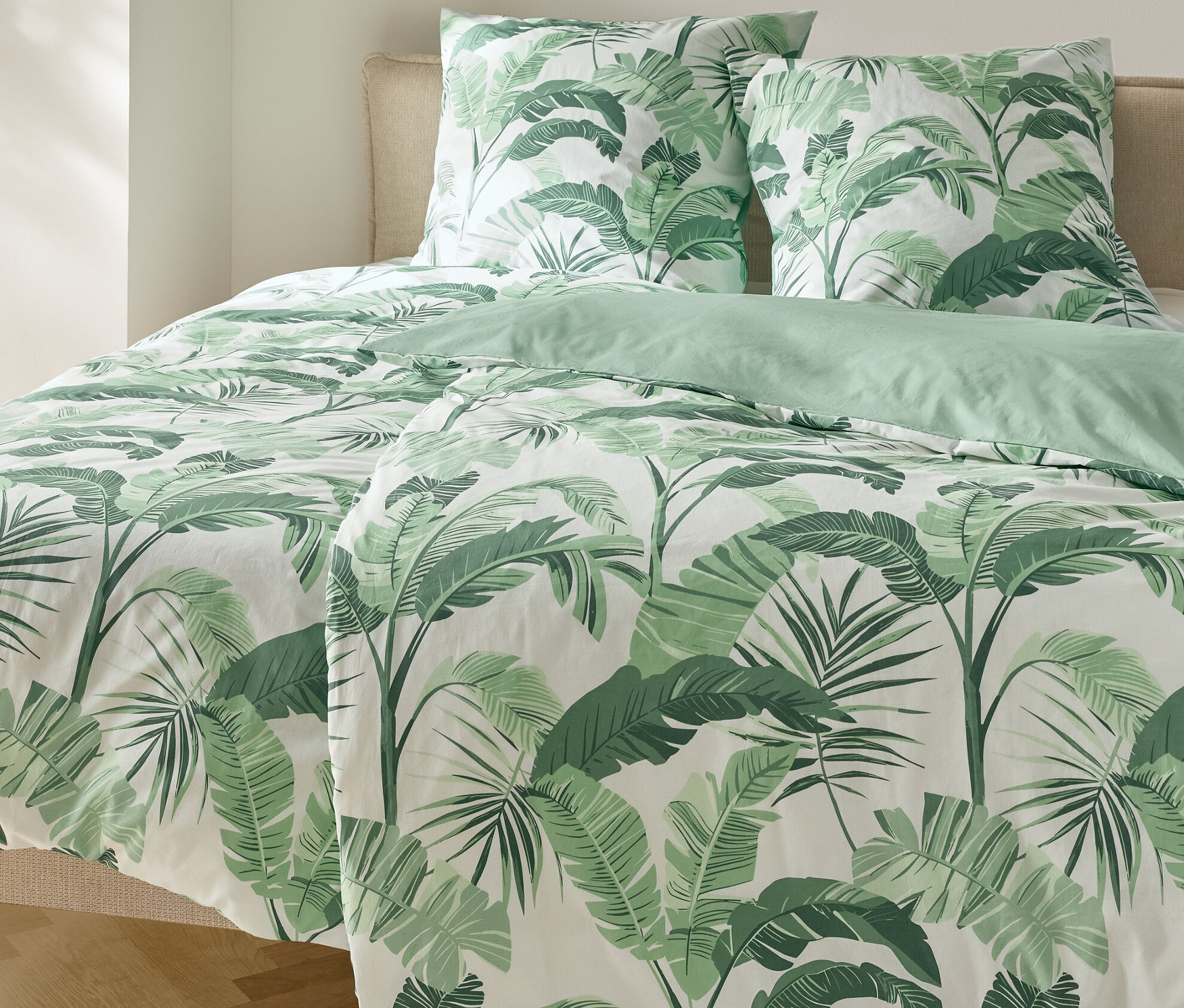 Łóżko z pościelą renforcé w palmy i dwiema poduszkami.