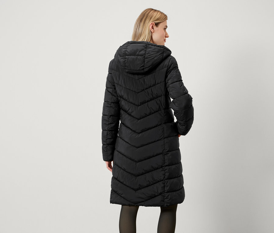 Widok z tyłu kobiety w długim, czarnym, pikowanym płaszczu z kapturem.