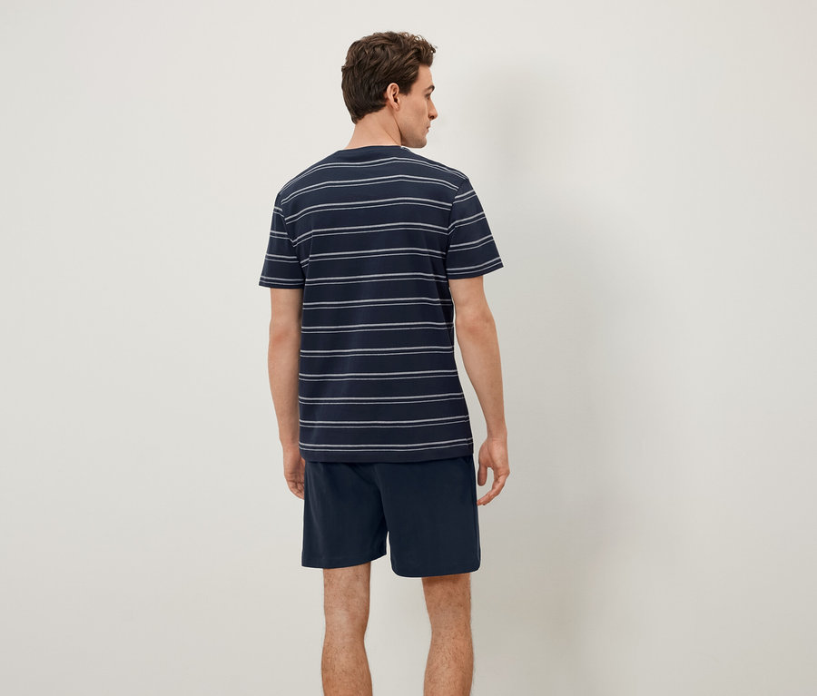 Mężczyzna tyłem do kamery ma na sobie koszulkę w paski i szorty.