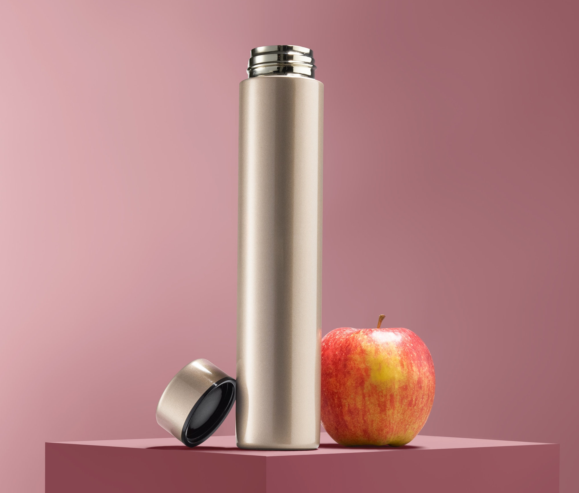 Butelka na napoje stoi obok jabłka, nakrętka leży obok.