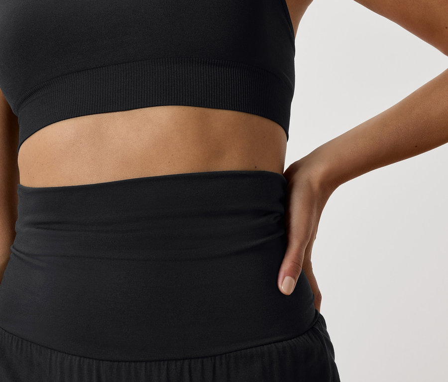 Zbliżenie na kobietę w czarnym staniku sportowym i czarnych szortach sportowych.