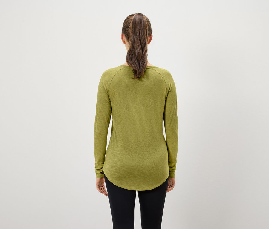 Widok z tyłu kobiety z brązowymi włosami związanymi w kucyk, ubranej w oliwkowozieloną koszulkę z długim rękawem i czarne legginsy.