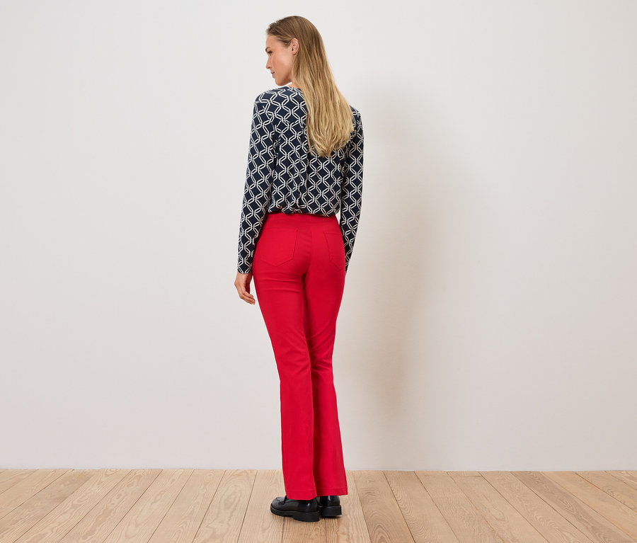 Kobieta stoi tyłem, ubrana w bluzkę we wzory i czerwone spodnie.