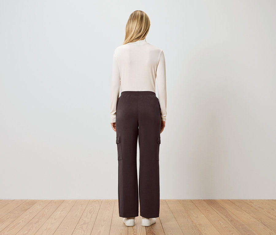 Widok z tyłu kobiety o blond włosach w kremowym golfie, brązowych spodniach cargo i białych tenisówkach.