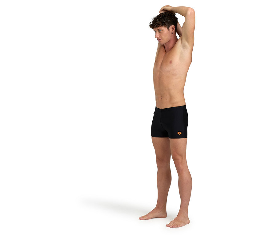 Mężczyzna rozciąga się, ubrany w czarne kąpielówki.