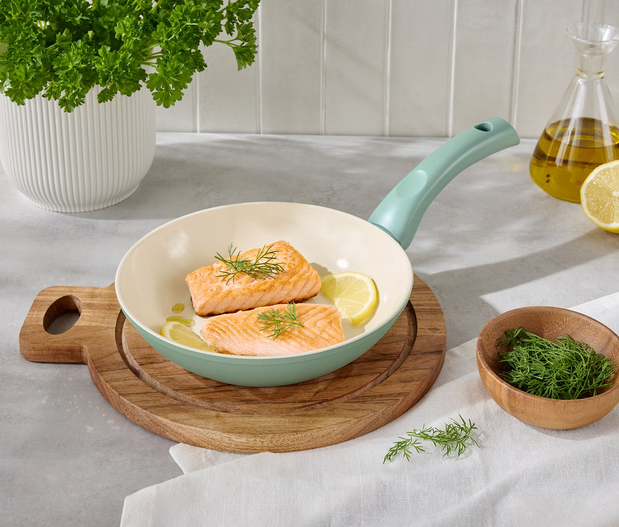 Dwa filety łososia z cytryną i koperkiem na patelni na drewnianej desce.