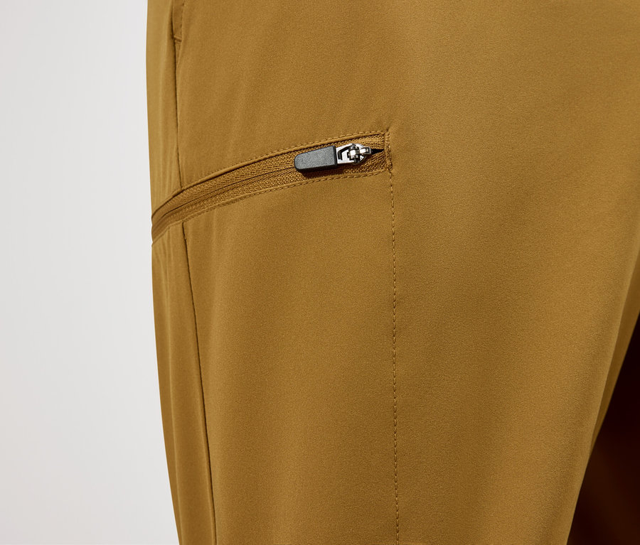 Zbliżenie na parę spodni w kolorze ochry z kieszenią zapinaną na zamek błyskawiczny.