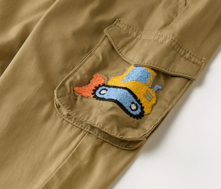 Zbliżenie na parę khaki spodni cargo z naszytą kieszenią ozdobioną haftowaną koparką w kolorze pomarańczowym, żółtym i niebieskim.