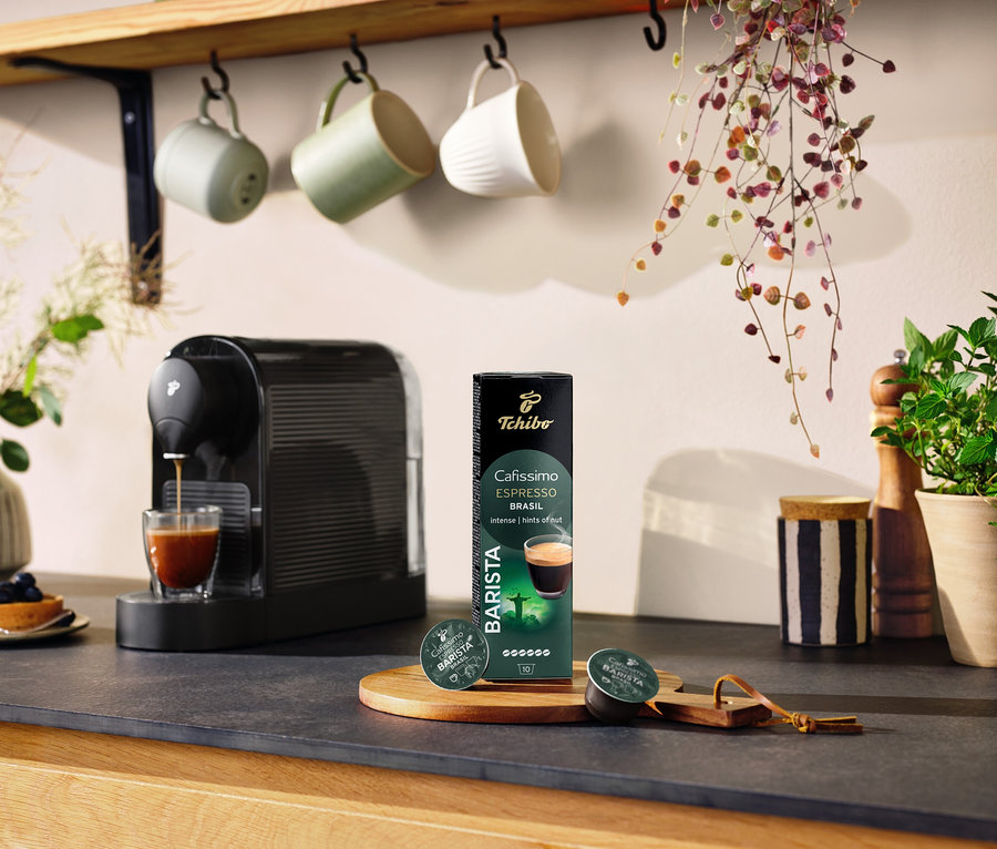 Czarny ekspres do kawy przygotowuje kawę do szklanki obok opakowania kapsułek BARISTA Espresso Brasil – 10 kapsułek.