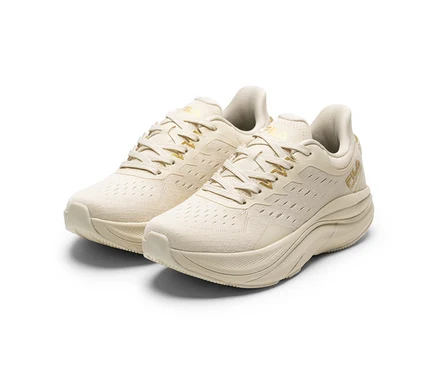 Dwa kremowe sneakersy z grubymi podeszwami i złotymi detalami, ustawione na białym tle.
