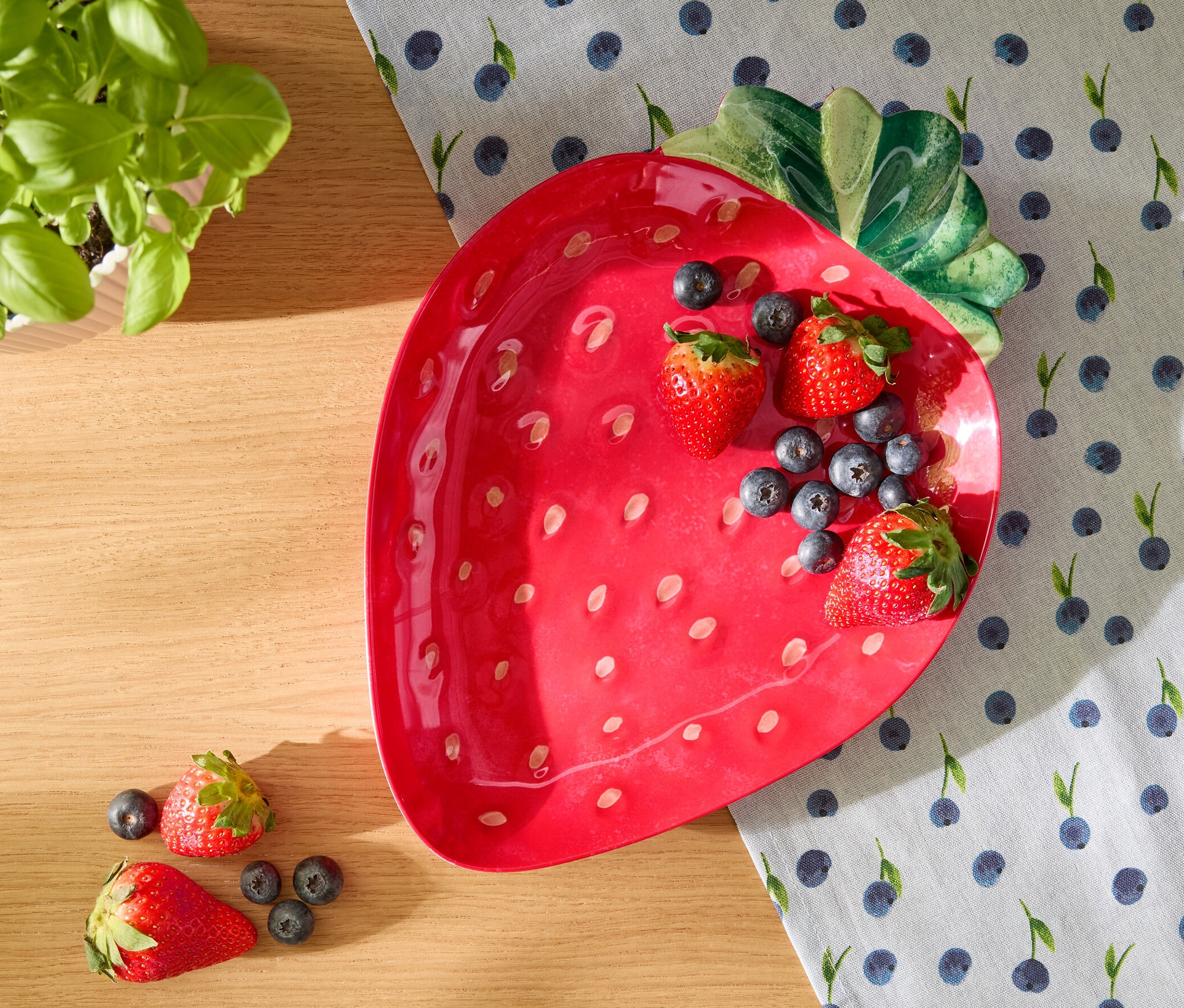 Czerwony talerz do serwowania w kształcie truskawki z truskawkami i jagodami na obrusie w jagody.