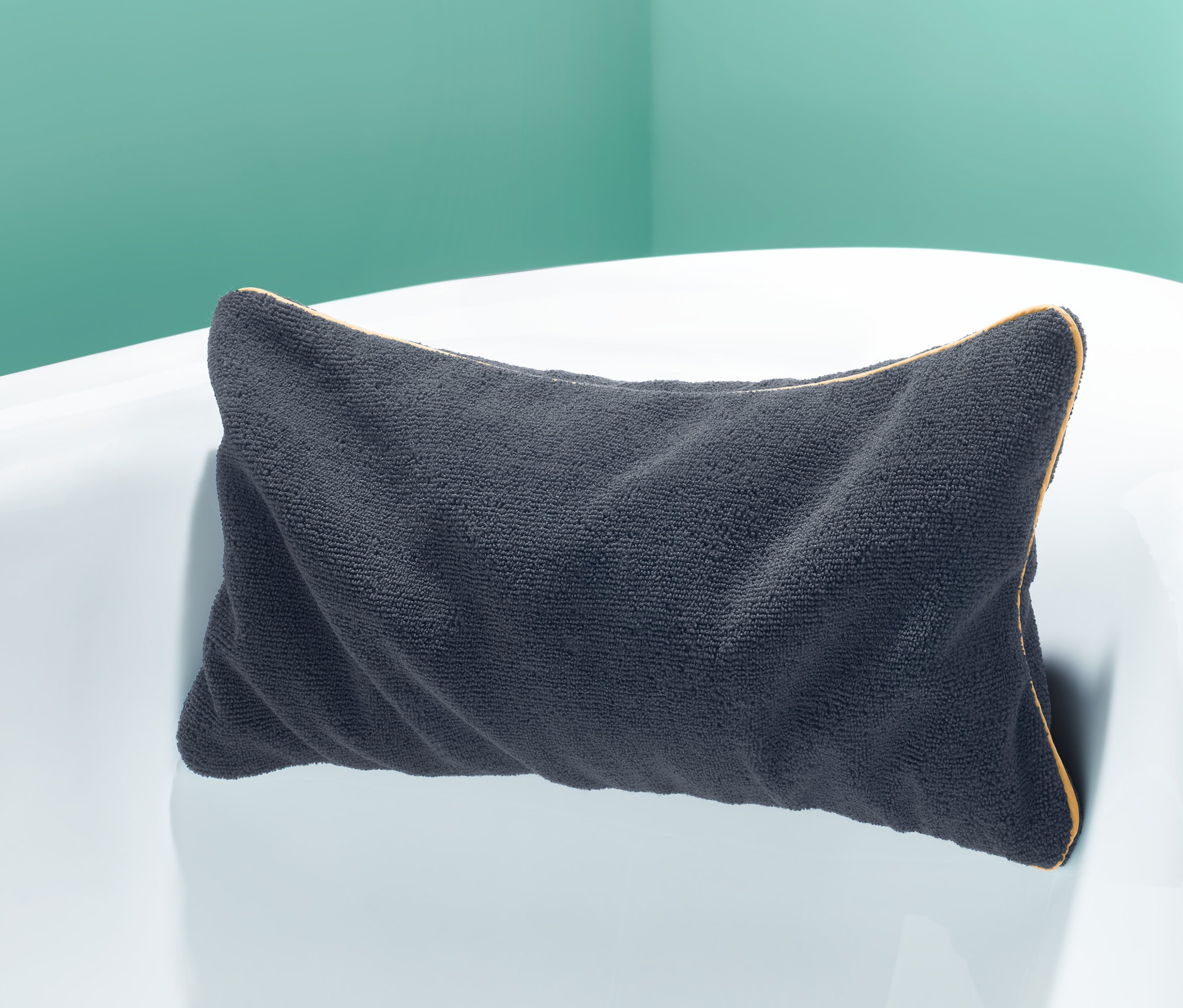 Antracytowa poduszka do wanny leży na krawędzi białej wanny.